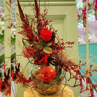 Arranjo de rosas vermelhas preservadas e secas em vaso de vidro com detalhes decorativos em Ikebana Flores